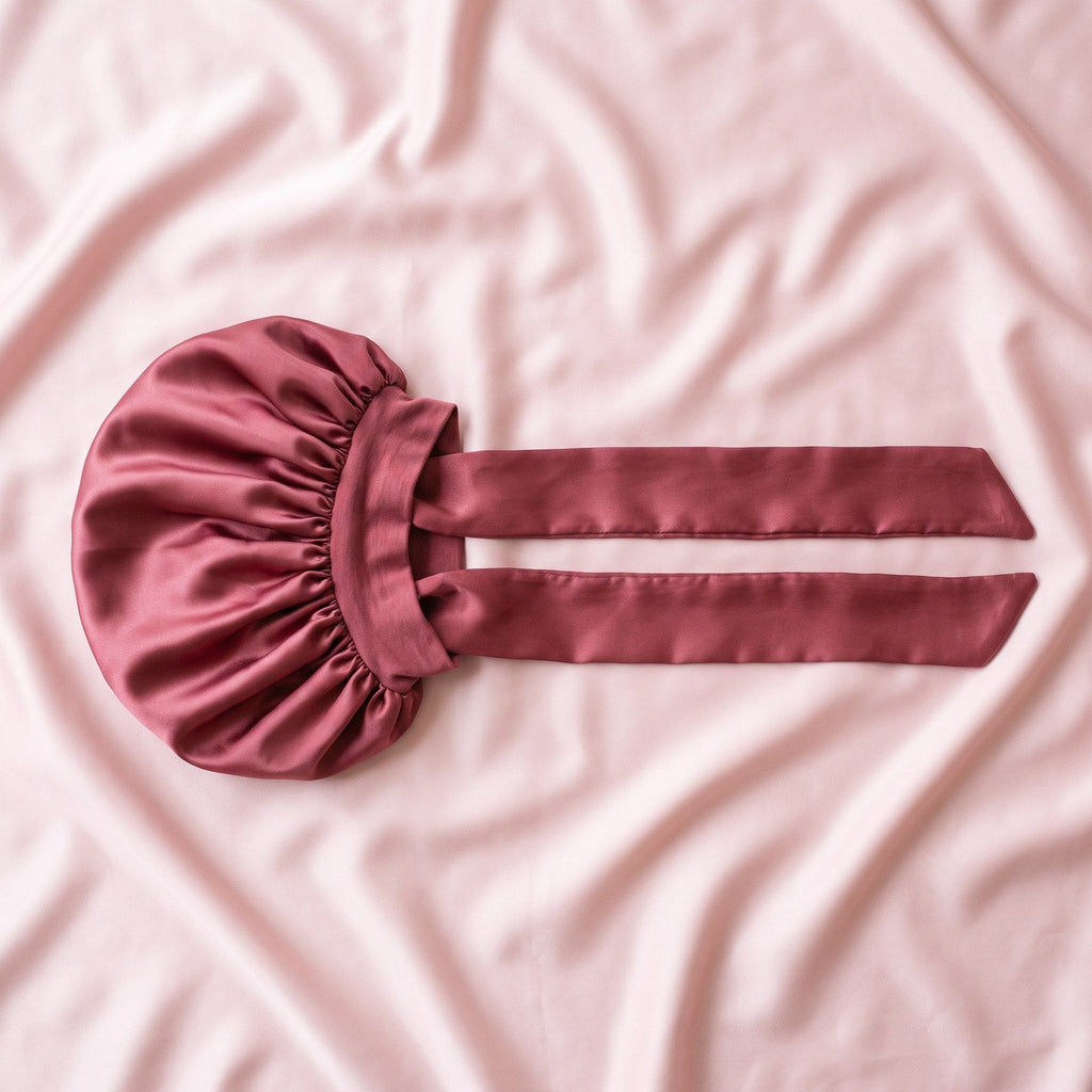 The satin bonnet laid flat on satin, its long tie band fully extended.