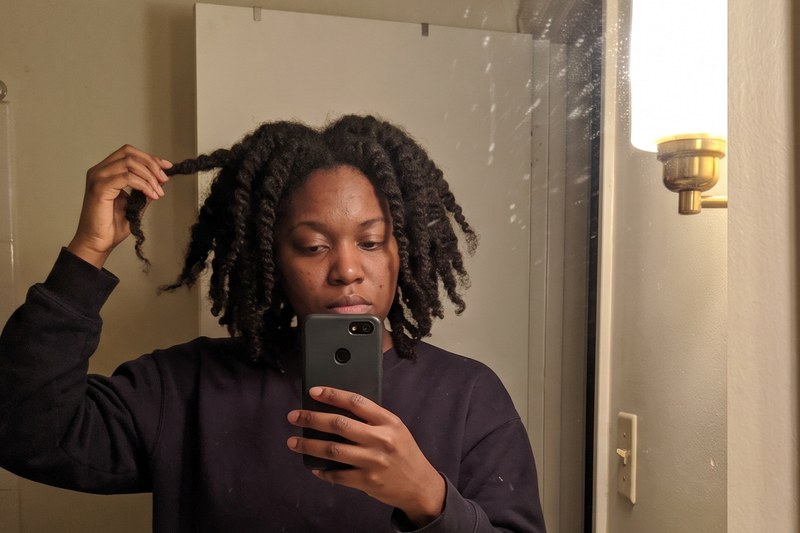 A woman with a 4c twist-out checks her hair in the bathroom mirror at night.