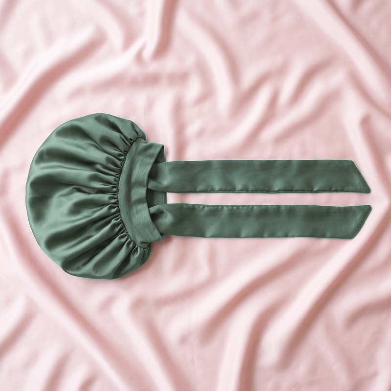 The satin bonnet laid flat on satin, its long tie band fully extended.