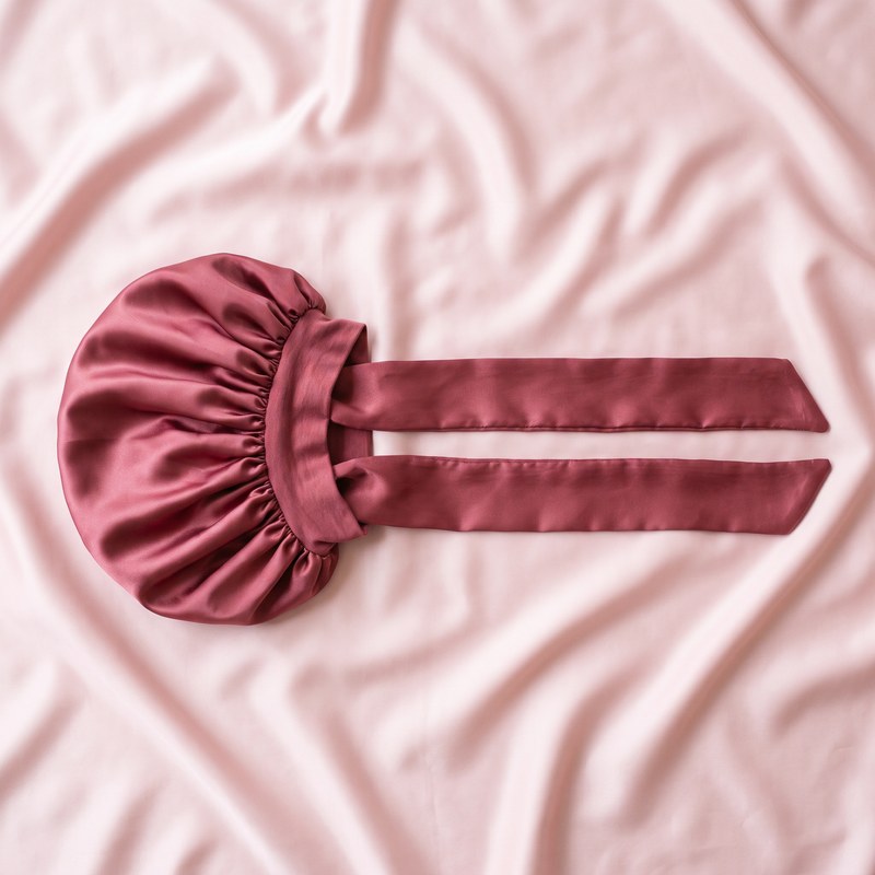 The satin bonnet laid flat on satin, its long tie band fully extended.