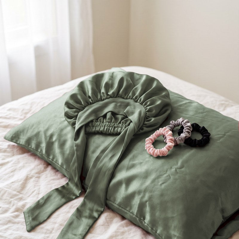The untied satin bonnet and satin scrunchies on a satin pillowcase in morning light.