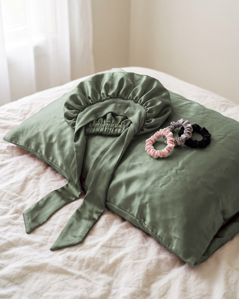 The untied satin bonnet and satin scrunchies on a satin pillowcase in morning light.